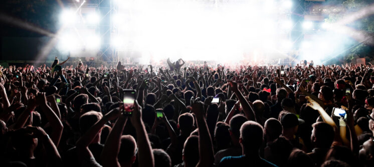 Back view of excited audience with arms raised cheering in front of the stage at music concert. Copy space.